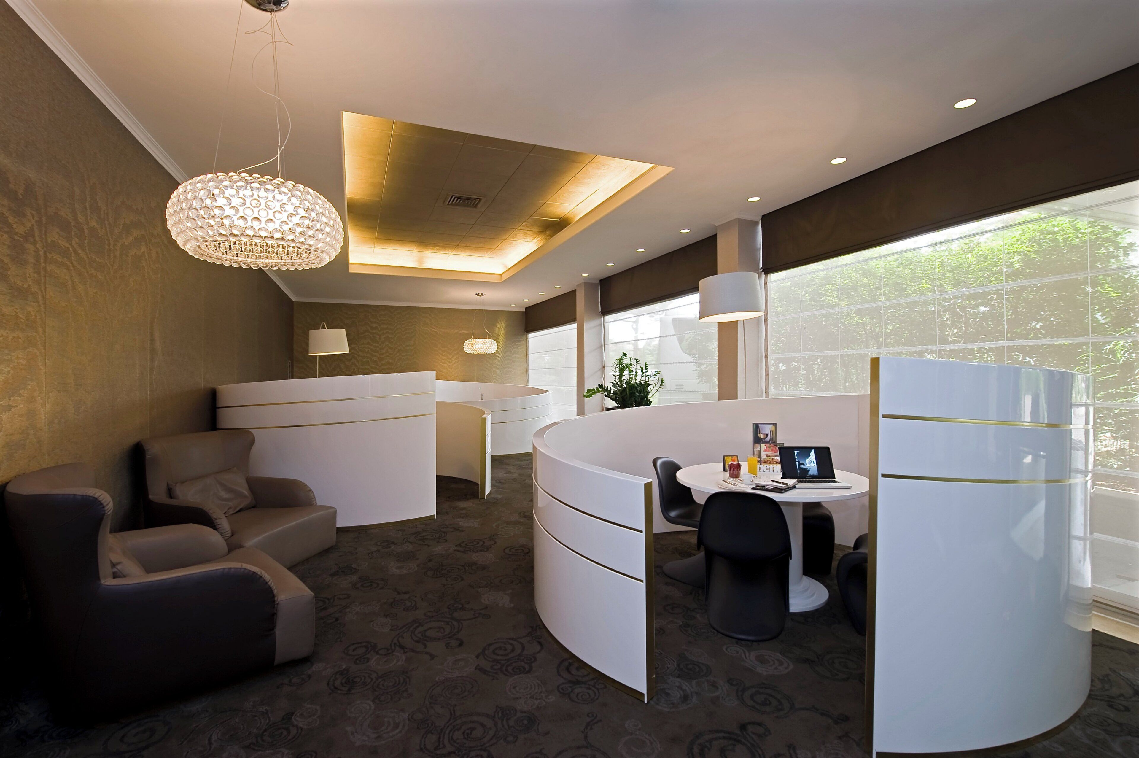 A modern hotel room with a curved seating area, a dining table, and a large window providing a view of the outdoors.