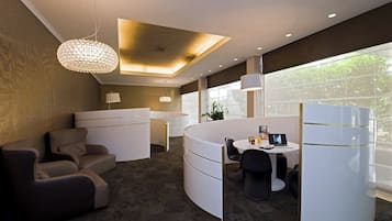 A modern hotel room with a curved seating area, a dining table, and a large window providing a view of the outdoors.