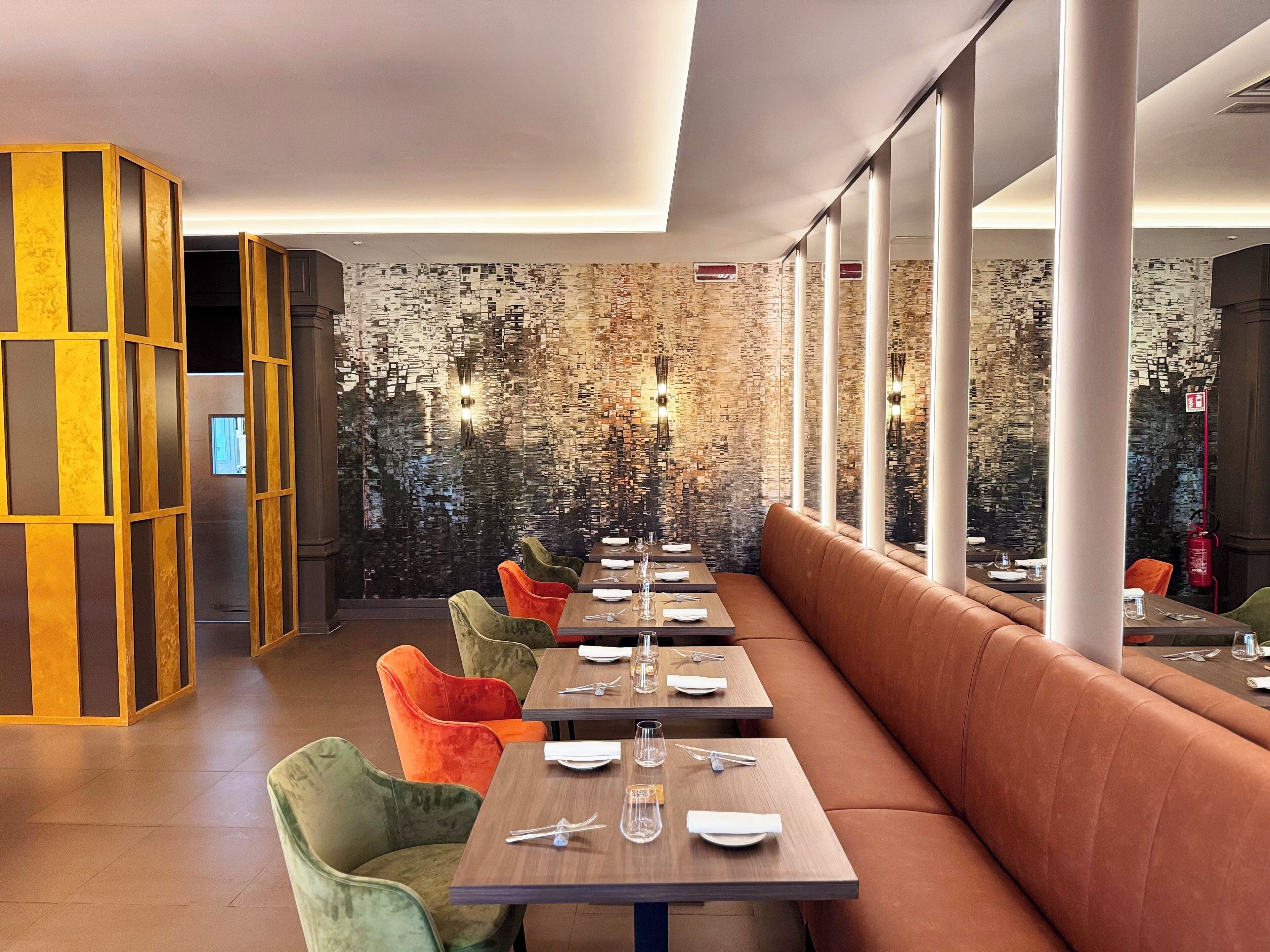 A modern restaurant interior with a long wooden table, cushioned seating, and a textured wall.