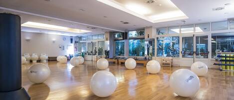A spacious gym with exercise balls, wooden flooring, and large windows.
