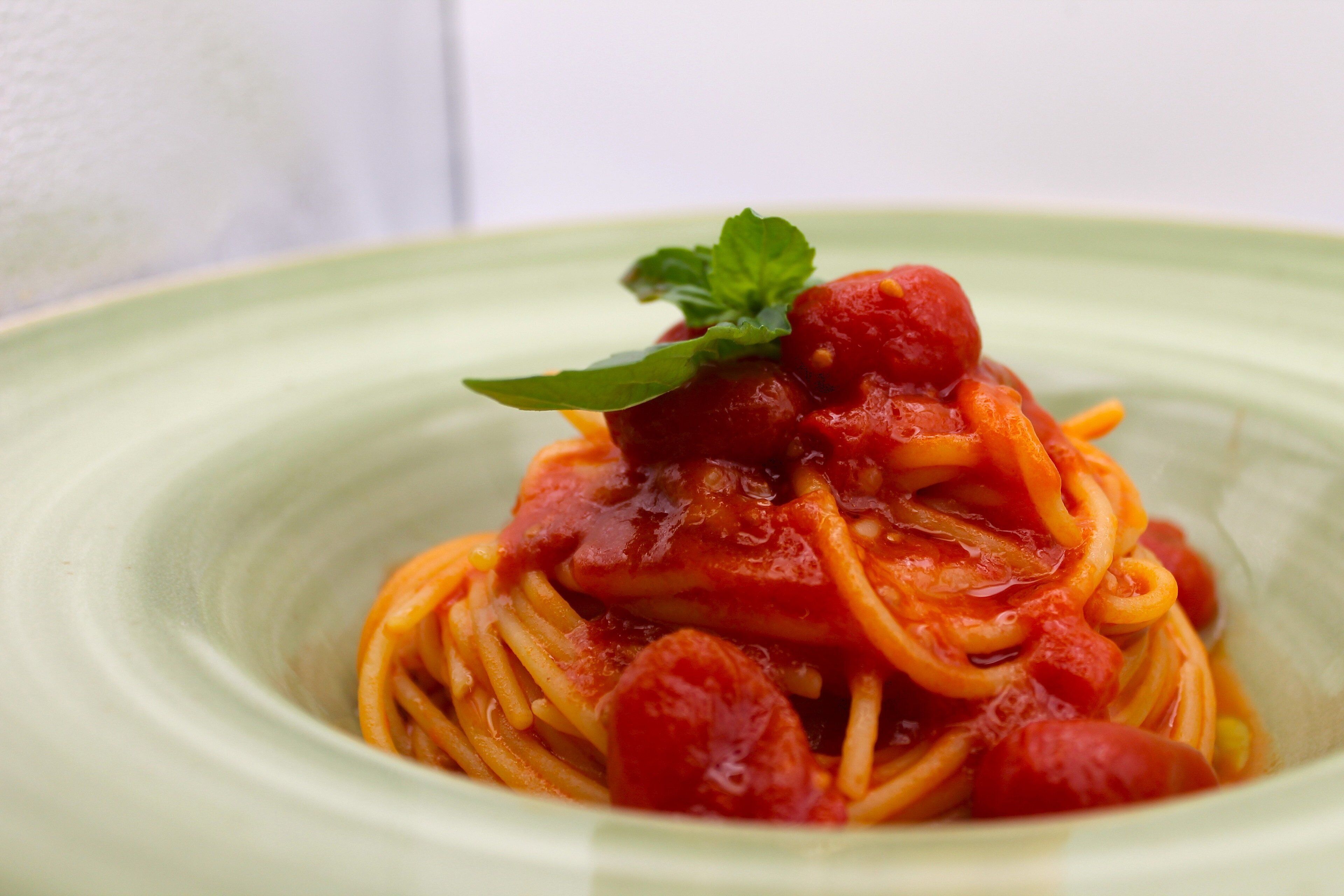 A plate of spaghetti with tomato sauce and a garnish.