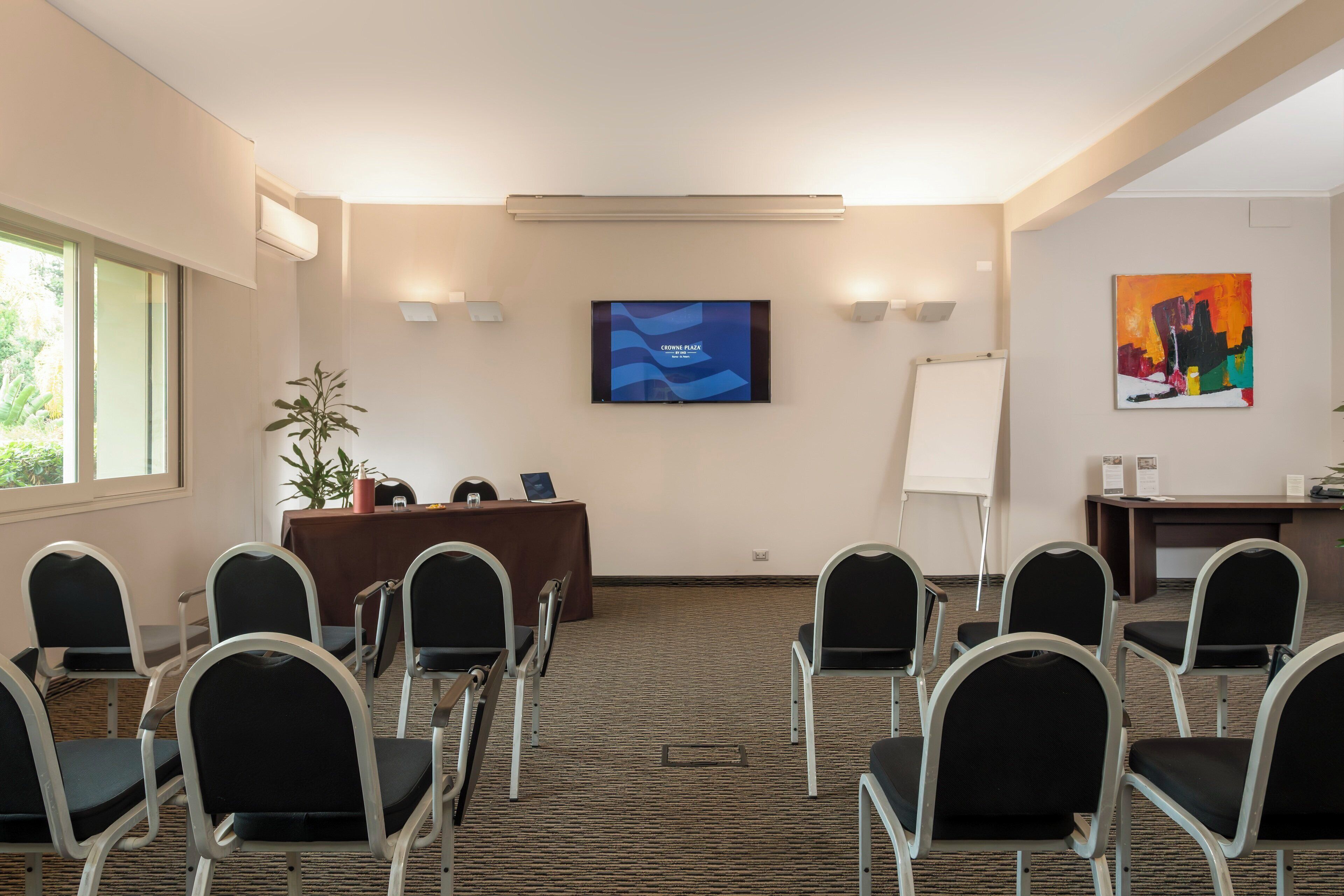 A conference room with a large screen, a whiteboard, and a desk with a computer.