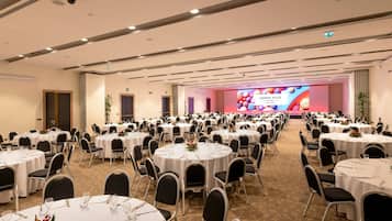 Une salle de conférence équipée de plusieurs tables rondes, de chaises noires et d’une scène avec un écran de présentation.