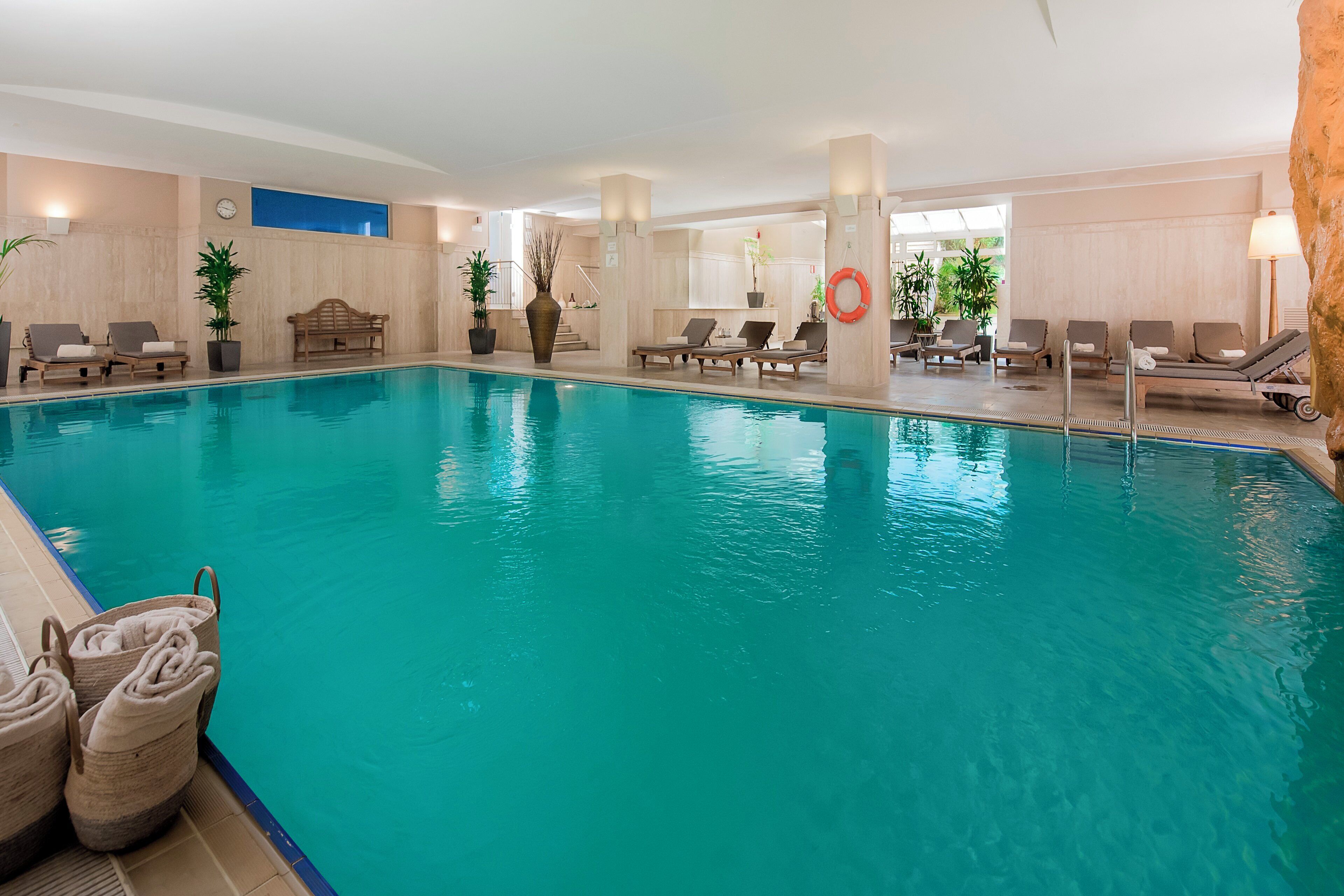 An indoor swimming pool with lounge chairs and potted plants.