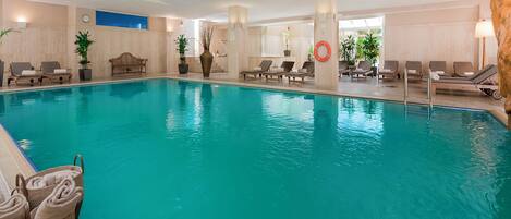 An indoor swimming pool with lounge chairs and potted plants.