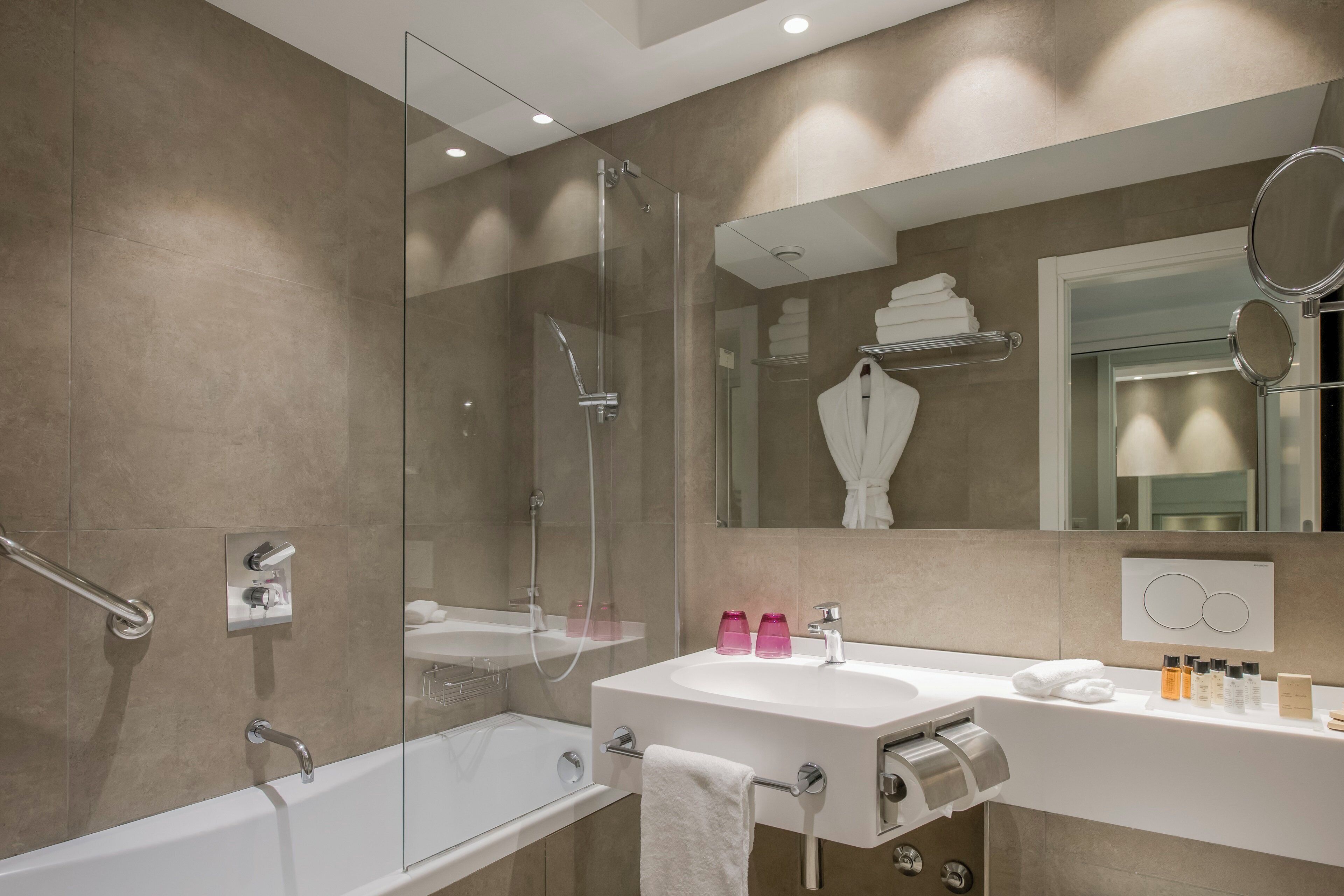 Un baño moderno con ducha envuelta en vidrio, una bañera blanca y un tocador con espejo.