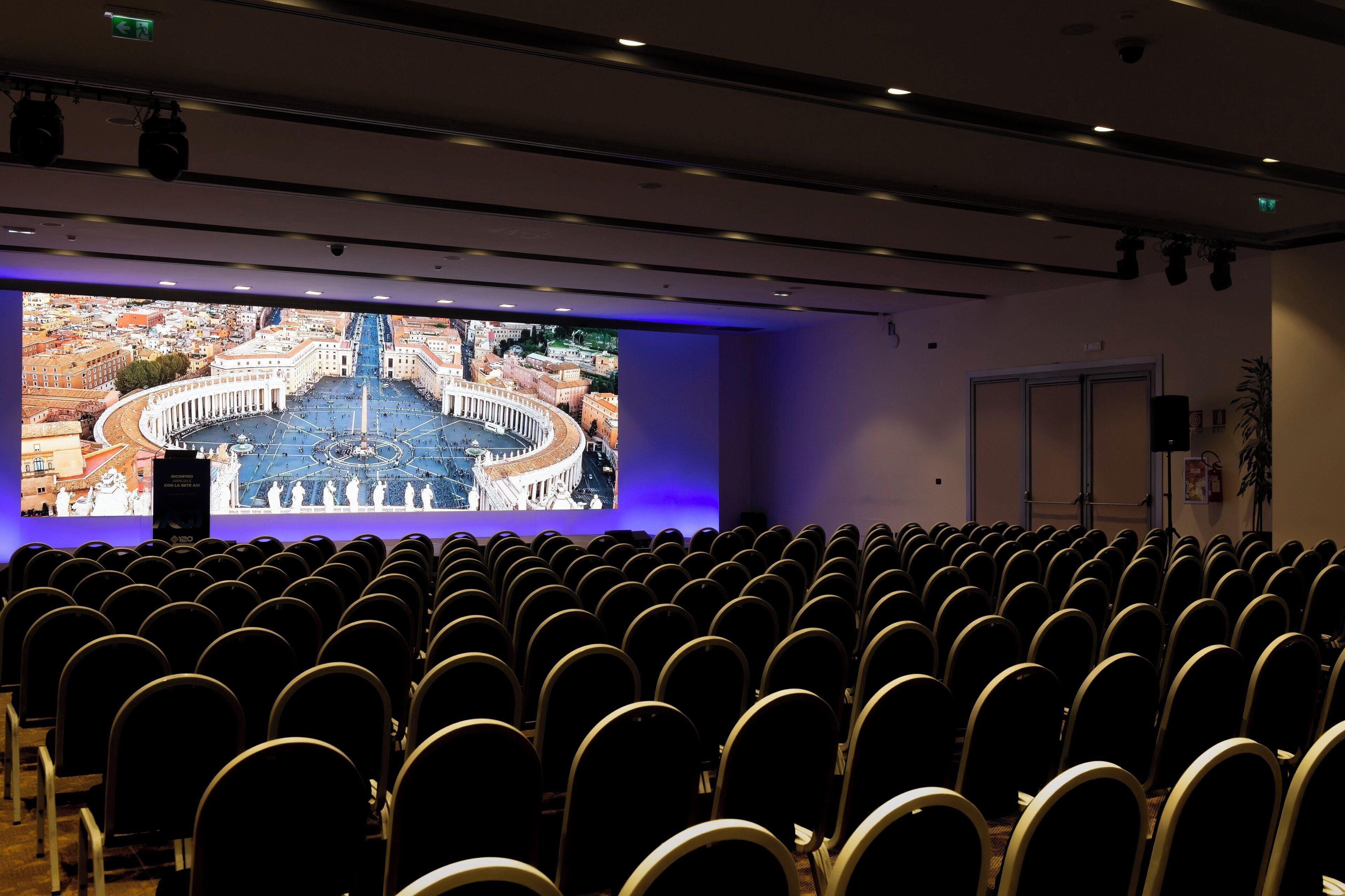 A conference room with rows of chairs facing a large screen displaying an image of a historical building.