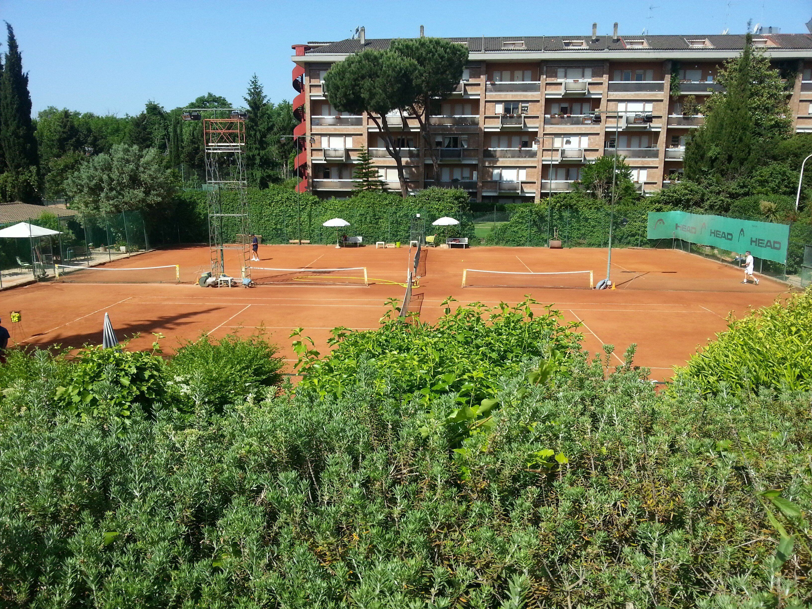 Un campo da tennis circondato dal verde e un edificio a più piani con balconi.