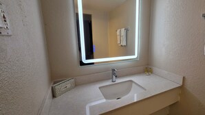 Un baño con un lavamanos blanco, un espejo, un perchero y un dispensador de toallas.