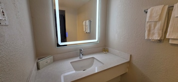 Un bagno con un lavandino bianco, uno specchio, un portasciugamani e un distributore di asciugamani.