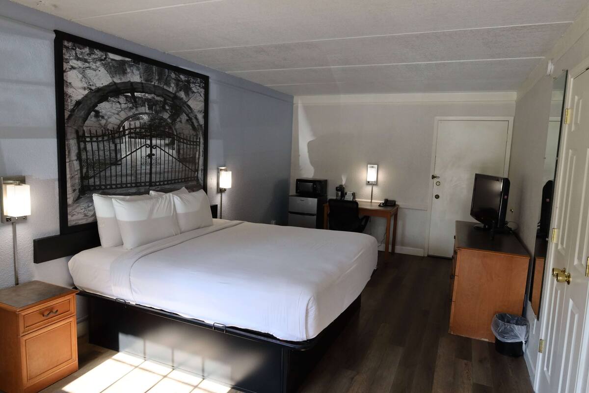 A hotel room with a bed, bedside lamps, a desk with a computer, a television, and a door.