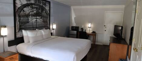 A hotel room with a bed, bedside lamps, a desk with a computer, a television, and a door.