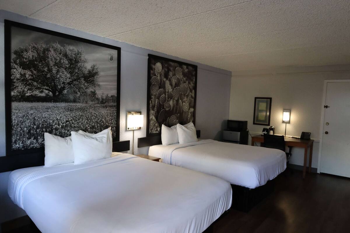 A hotel room with two beds, a desk, a chair, and two wall-mounted lamps.
