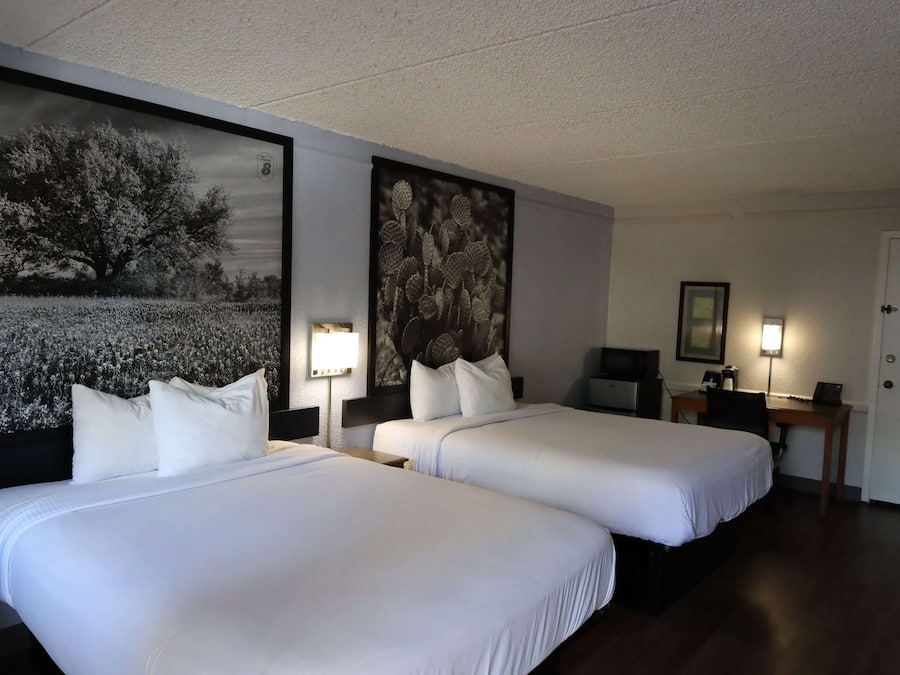 A hotel room with two beds, a desk, a chair, and two wall-mounted lamps.