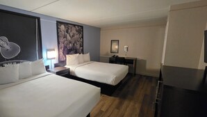 Habitación de hotel con dos camas, un escritorio, una silla, una lámpara y una obra de arte con motivos de guitarra en la pared.