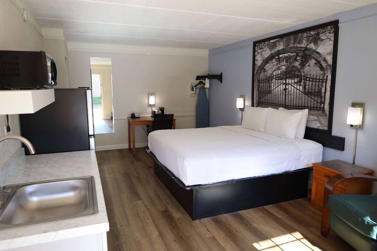 A compact hotel room with a bed, a small desk, a sink, and a mural on the wall.