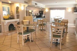 Zona pranzo con diverse sedie e tavoli di legno, pavimento piastrellato, angolo cottura con elettrodomestici e camino.