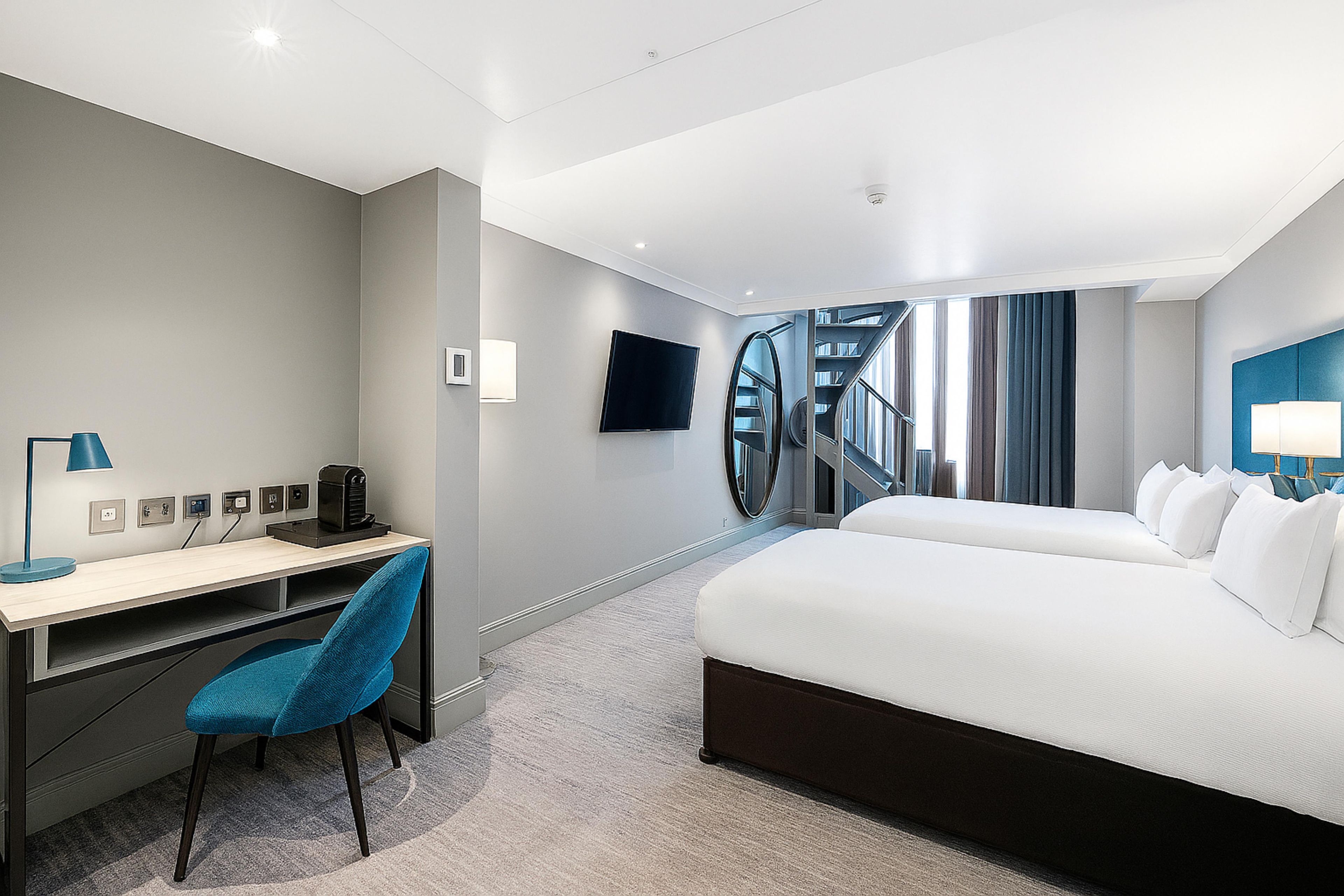 A hotel room with a bed, desk, chair, TV, and a staircase.