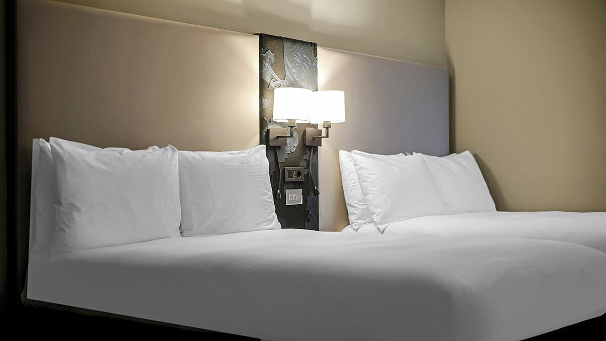 Habitació d'hotel amb un llit gran, dos coixins blancs i una làmpada penjada a la paret.
