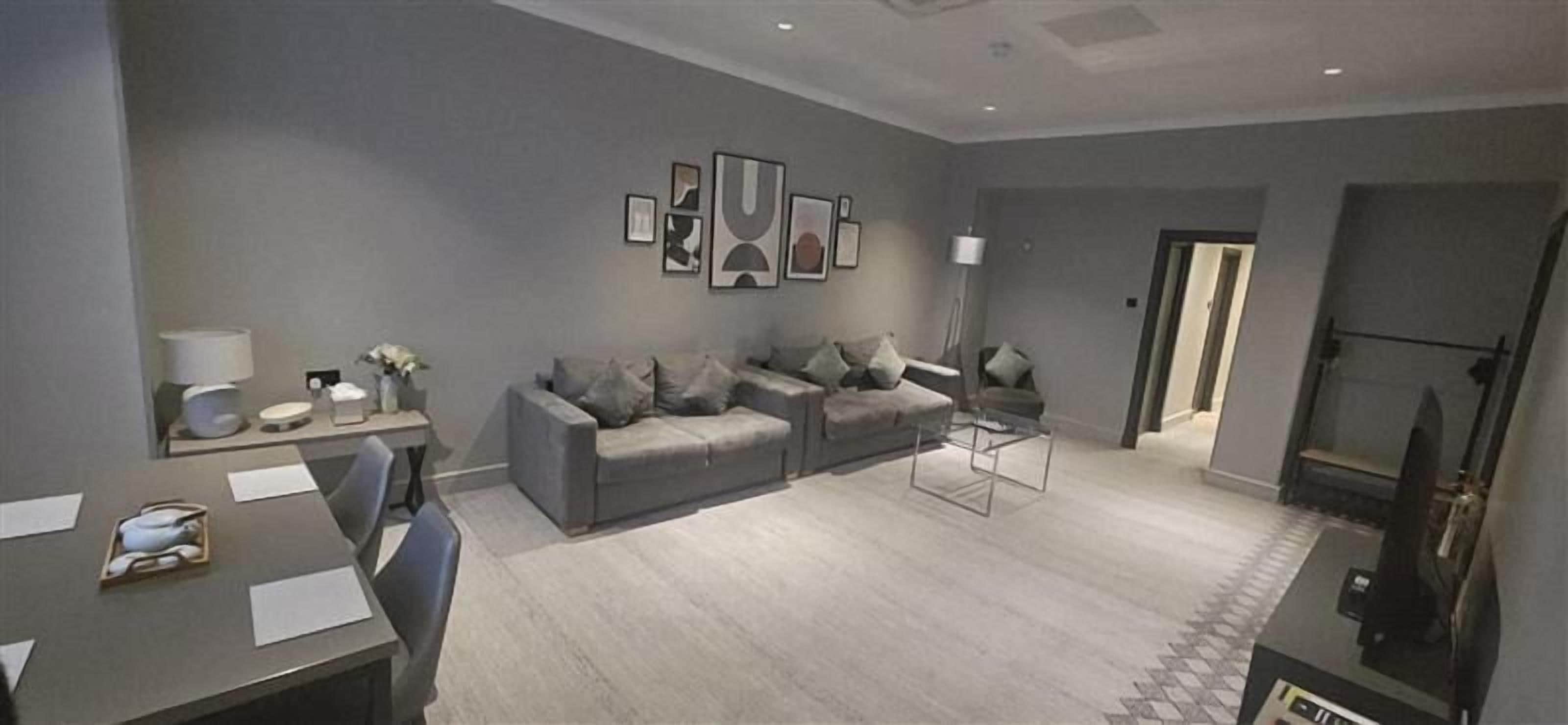 Ein modernes Wohnzimmer mit einer grauen Sofagarnitur, einem Esstisch mit Stühlen und einem Flachbildfernseher.