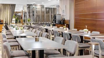 Een modern restaurant met meerdere eettafels en stoelen, een bar en een decoratieve glazen scheiding.