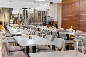 En modern restaurang med flera bord och stolar, en bardisk och en dekorativ glasvägg.