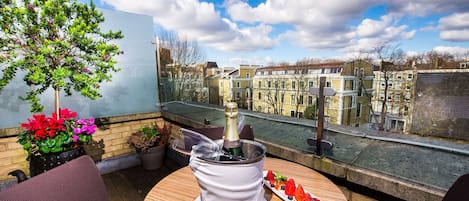 Eine Dachterrasse mit Champagnerkühlbox, Topfpflanzen und einer Obstplatte.