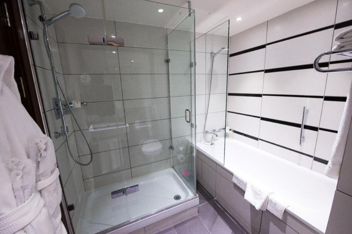 Un baño moderno con ducha de vidrio, una bañera blanca y un espejo grande con líneas horizontales negras.
