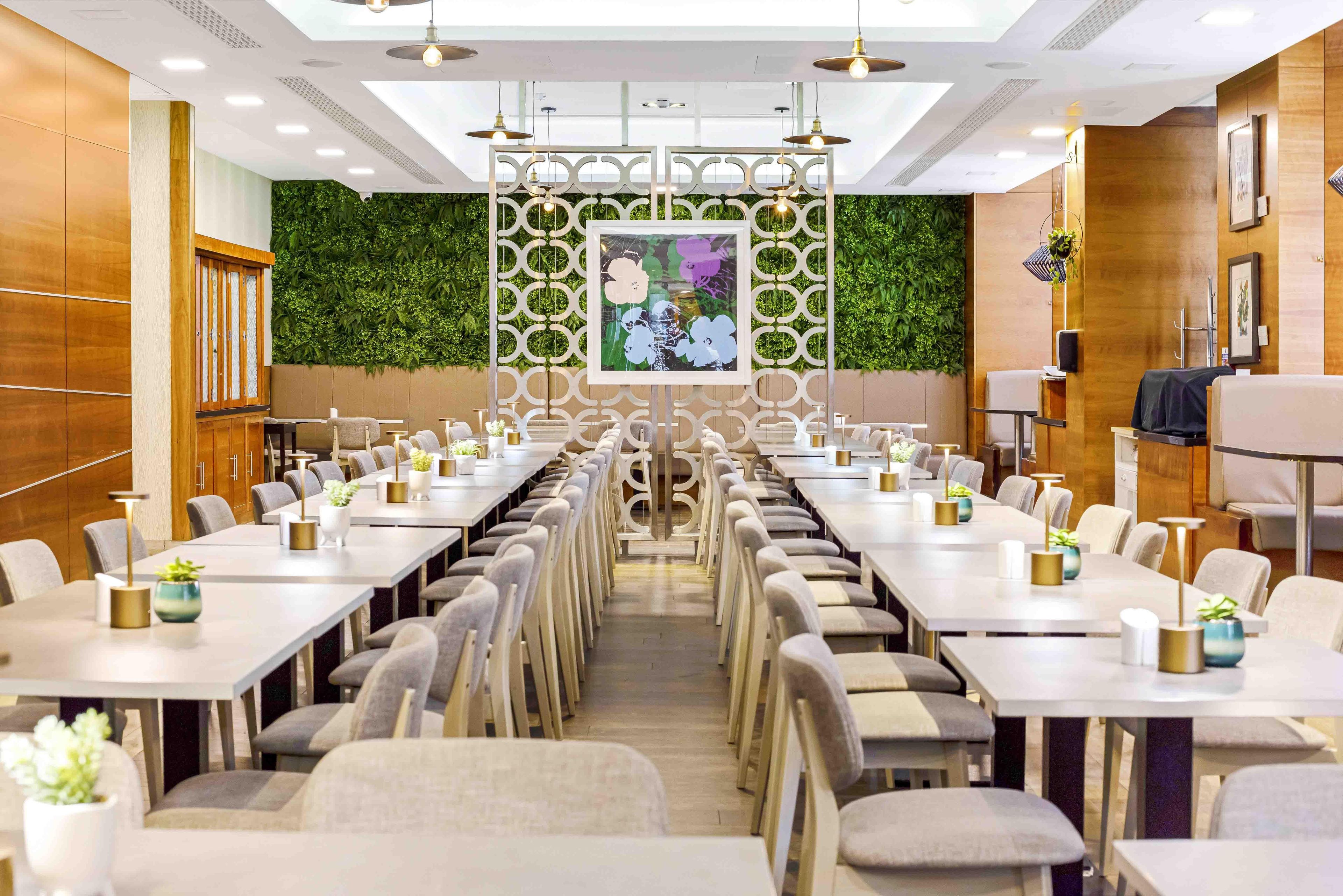 A conference room with long tables, chairs, and a decorative wall with greenery and a framed picture.