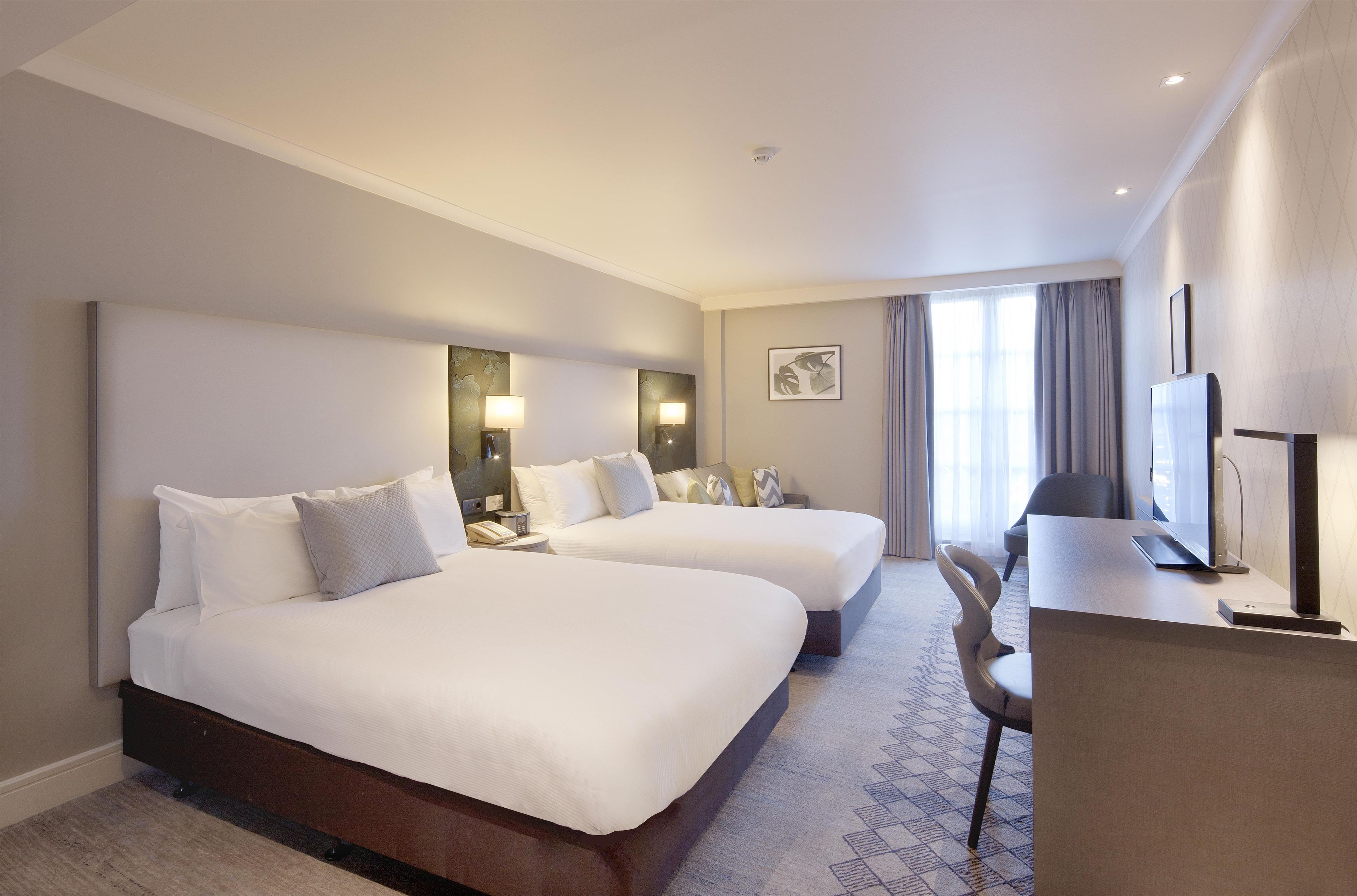 A hotel room with two beds, a desk with a computer, a chair, and a window with curtains.