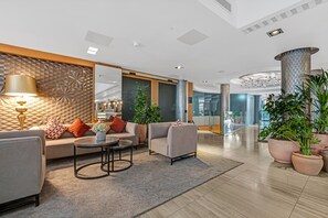 A modern lobby with a sofa, armchairs, a coffee table, and potted plants. - DoubleTree by Hilton London Kensington (London)