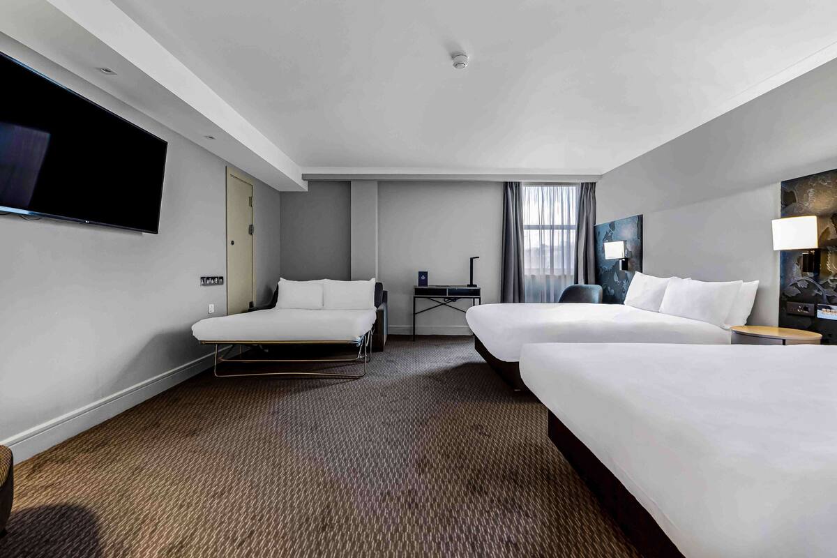 A hotel room with two beds, a flat-screen TV, a desk, and a chair.