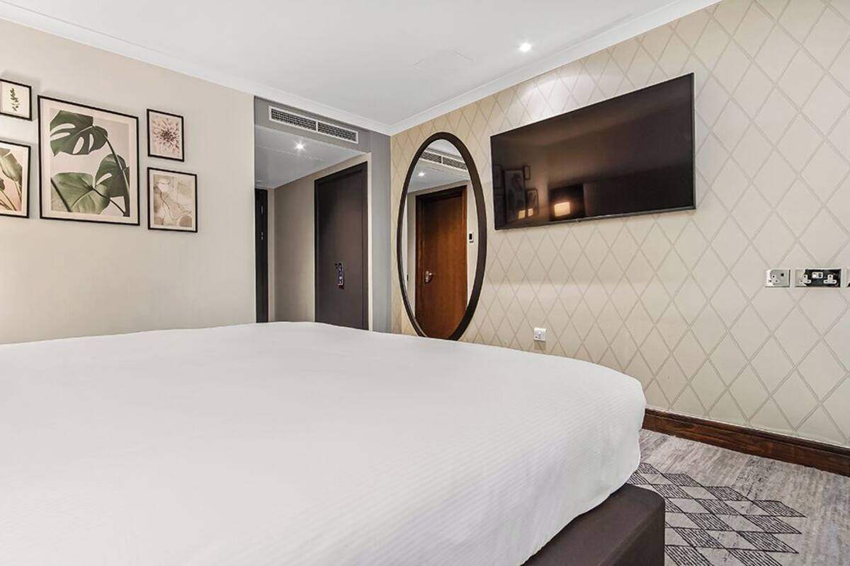 A hotel room with a large bed, framed botanical prints on the wall, a mirror, and a flat-screen TV.