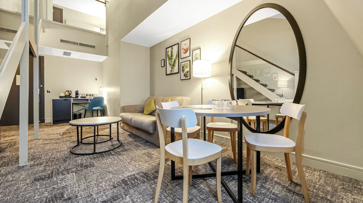Una habitación de hotel moderna con comedor, sofá y escalera.