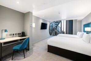 Une chambre d’hôtel avec un lit, un bureau, une chaise, une télévision et un escalier.