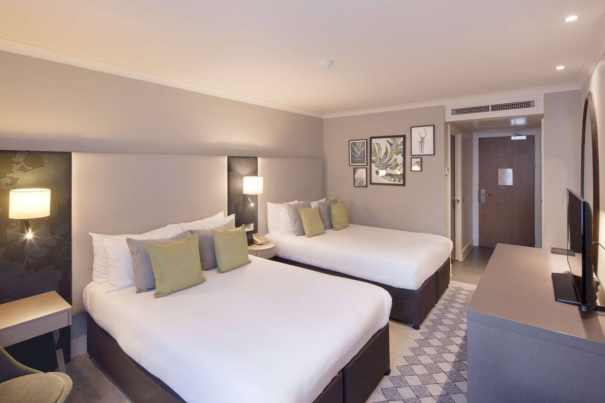 A hotel room with two beds, a desk, a chair, a TV, and framed pictures on the wall.
