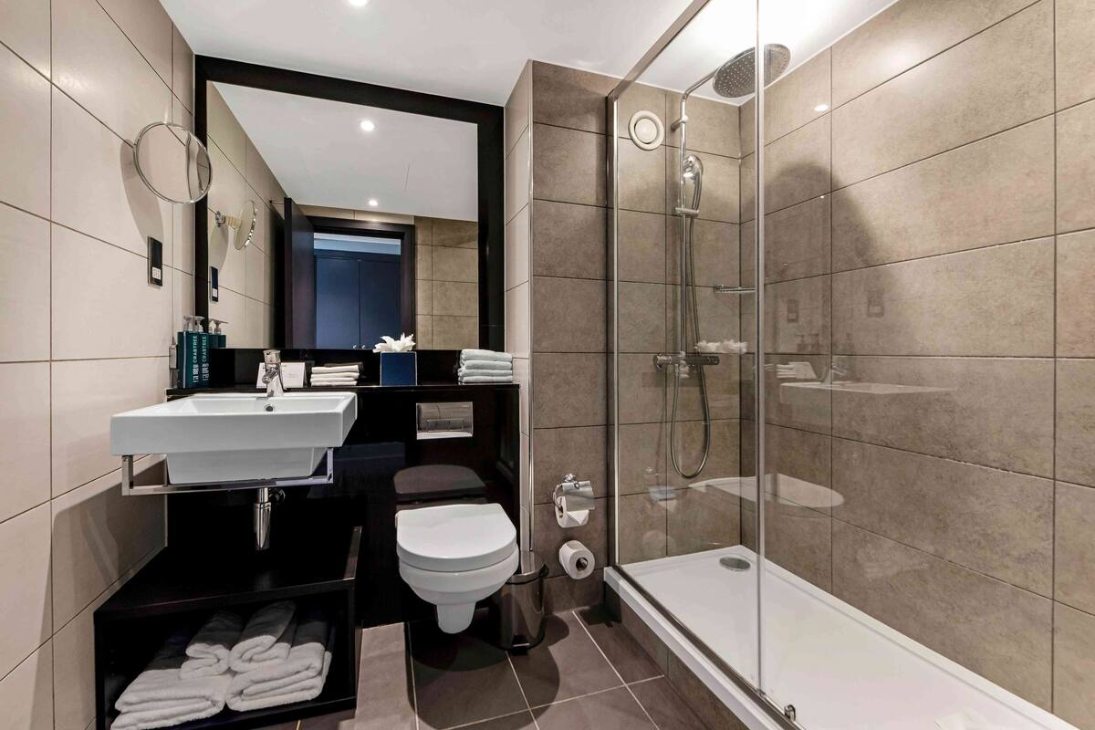 A modern bathroom with a glass-enclosed shower, a white sink, and a toilet.