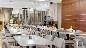 Un espace repas moderne comprenant plusieurs tables et chaises, un coin cuisine et une cloison en verre décorative.