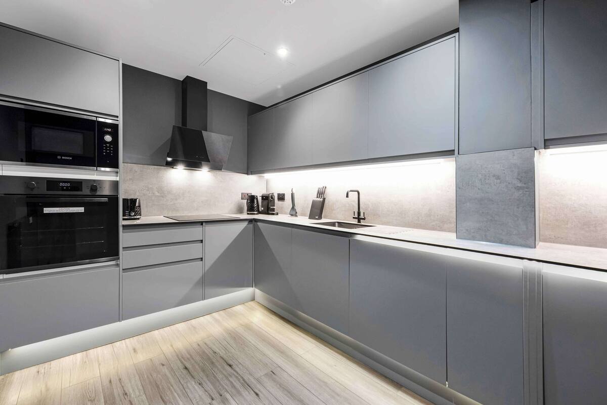 A modern kitchen with built-in appliances, grey cabinetry, and a wooden floor.