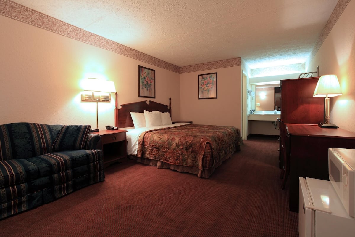 A hotel room with a bed, a sofa, a desk, a lamp, and a microwave.