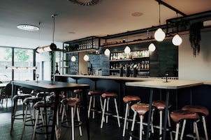 A bar area with stools, shelves of bottles, and hanging lights.