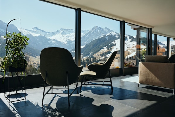 A modern room with large windows, a sofa, a chair, and a potted plant.