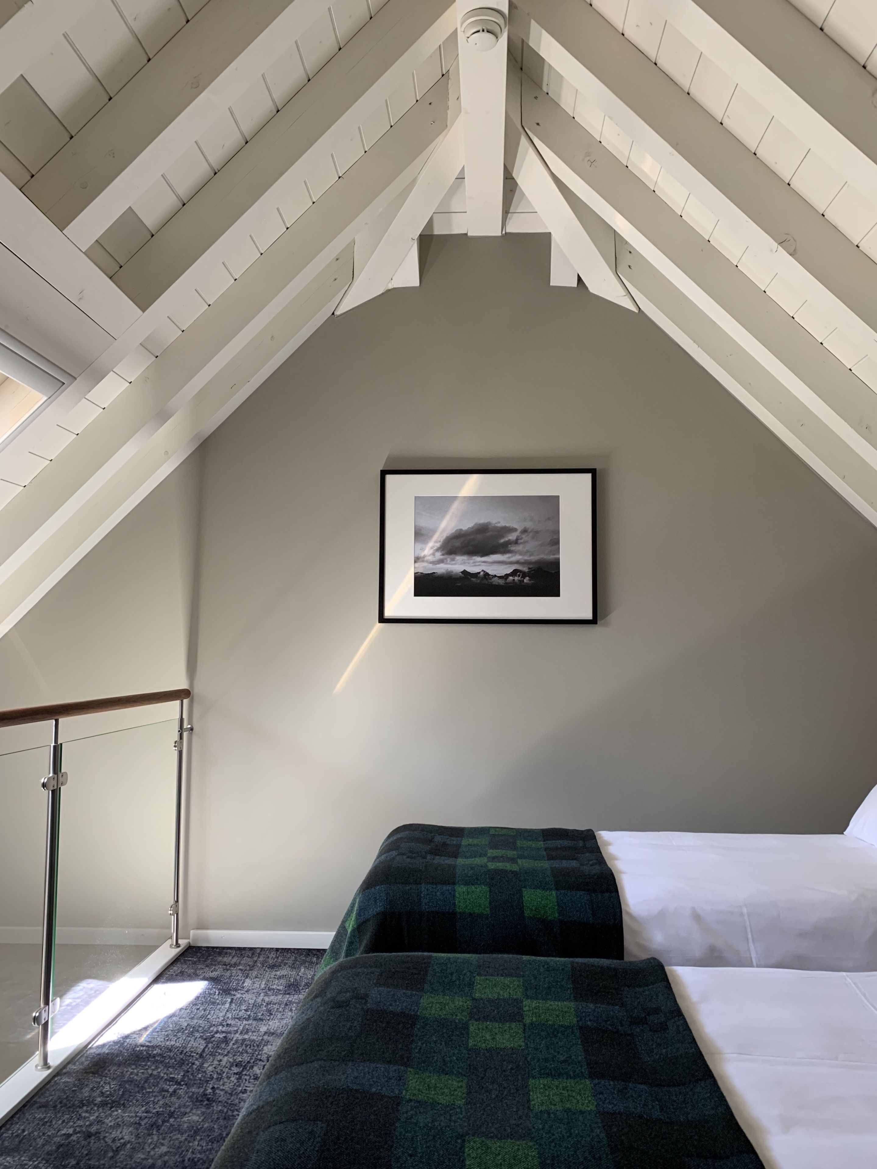 Ein Schlafzimmer mit schrägem Dach, einem gerahmten Foto an der Wand, einem Bett mit einer grün-schwarz karierten Decke und einer Glastür, die auf einen Balkon führt.