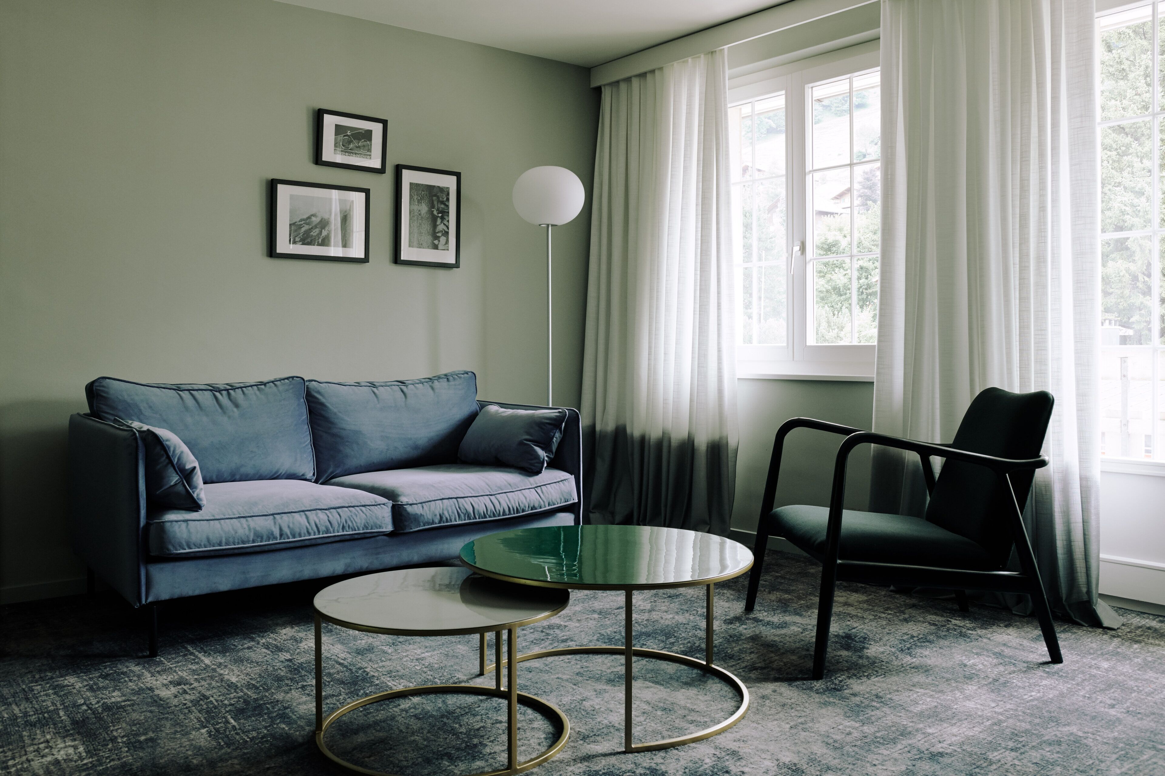 Una sala de estar con sofá, sillón, una mesa de centro y una lámpara de pie. Hay tres cuadros enmarcados en la pared.