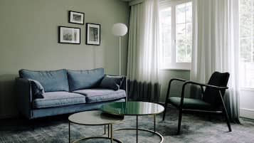Una sala de estar con sofá, sillón, una mesa de centro y una lámpara de pie. Hay tres cuadros enmarcados en la pared.