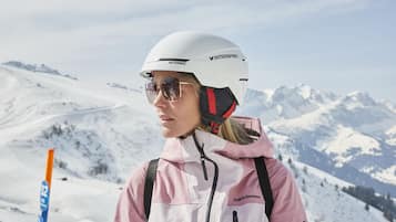 A person in a white helmet and pink jacket standing on a snowy mountain with a clear sky.