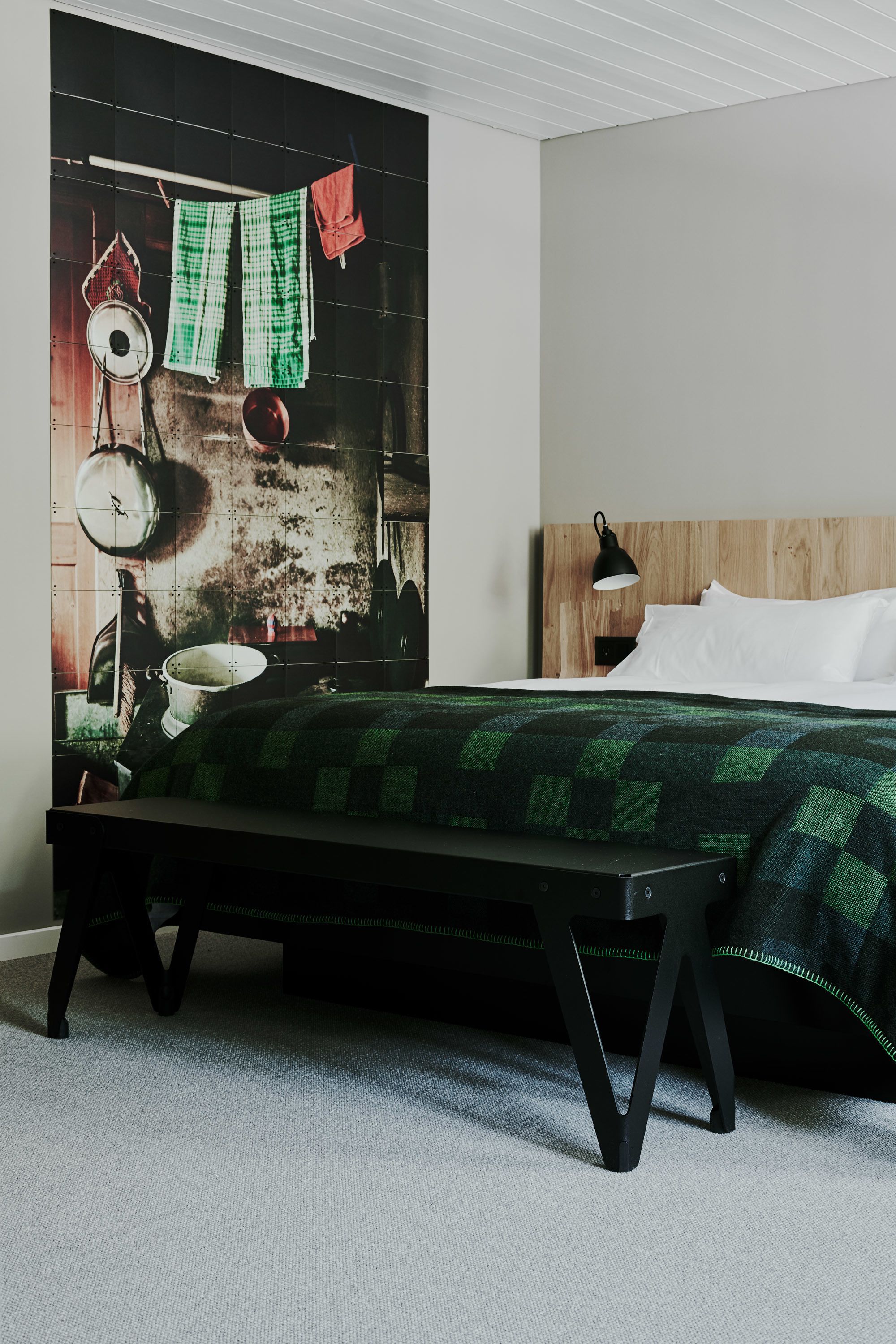 Un dormitorio con una cama, un banco, una lámpara de pared y un cabecero de madera.