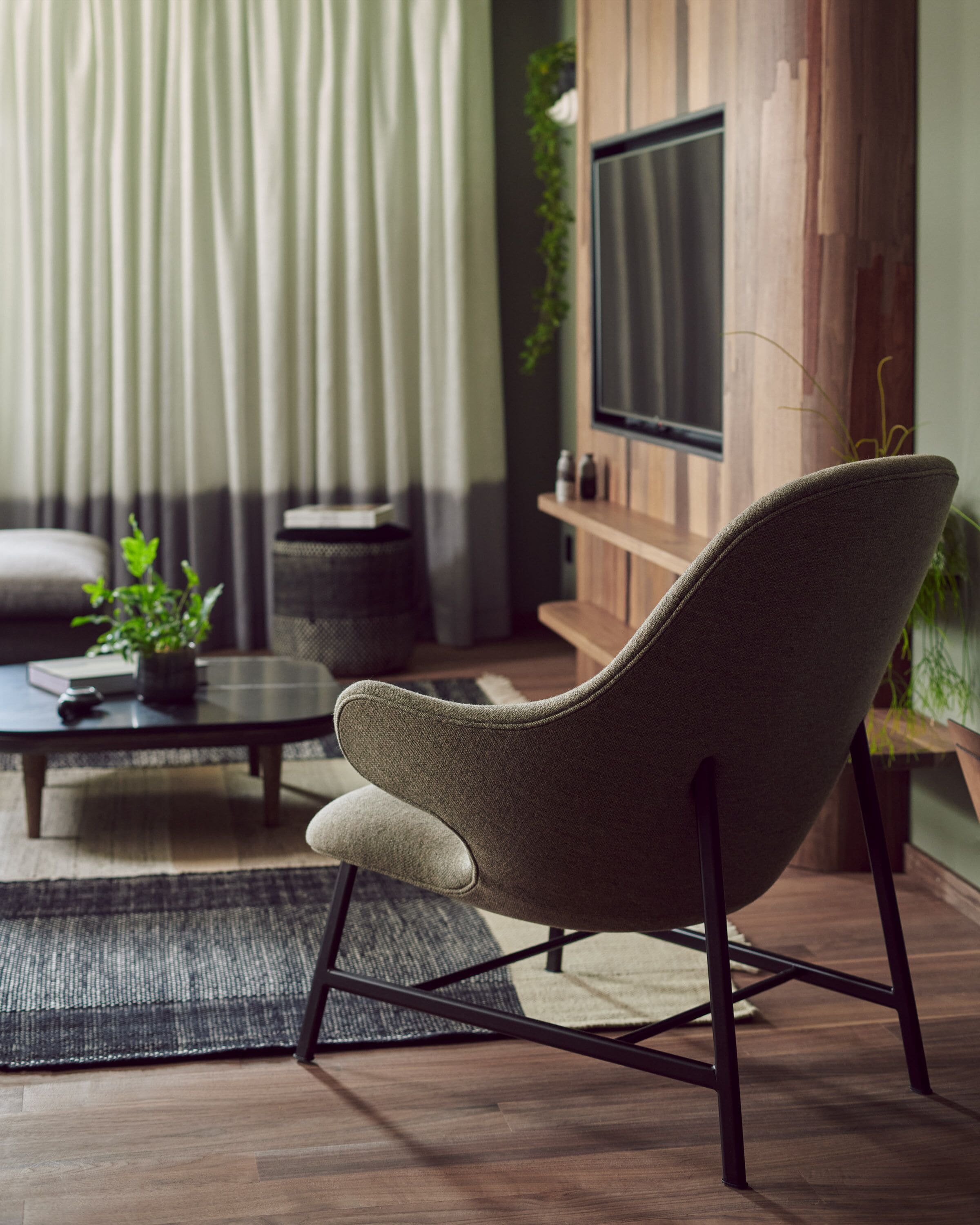 A modern living room with a dark wood floor, a grey armchair, a black coffee table, and a television mounted on a wooden wall.