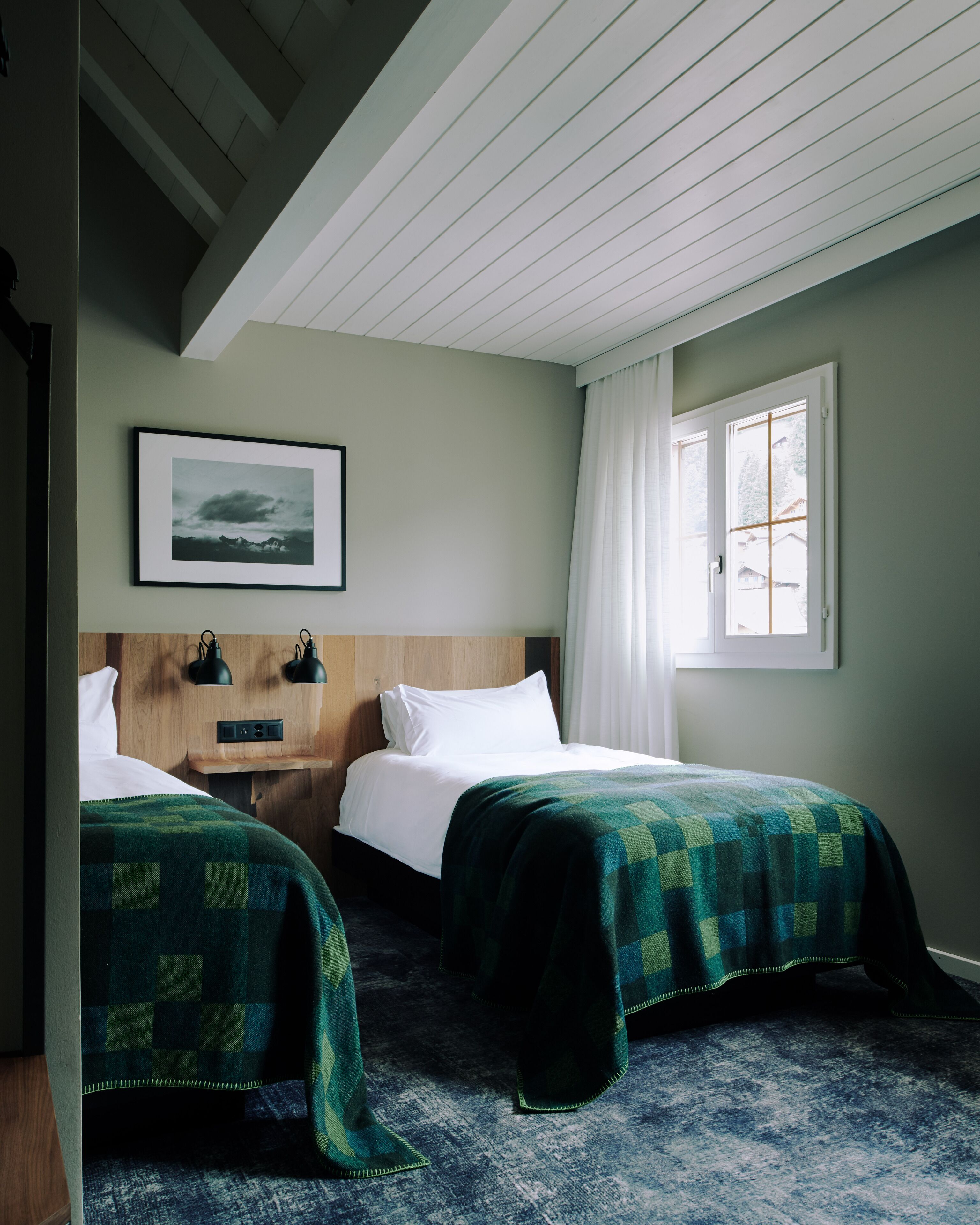 A hotel room with two beds, a wooden headboard, a framed picture on the wall, and a window with curtains.