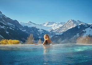 A person in a hot tub with a mountainous landscape in the background. - The Cambrian (Adelboden)